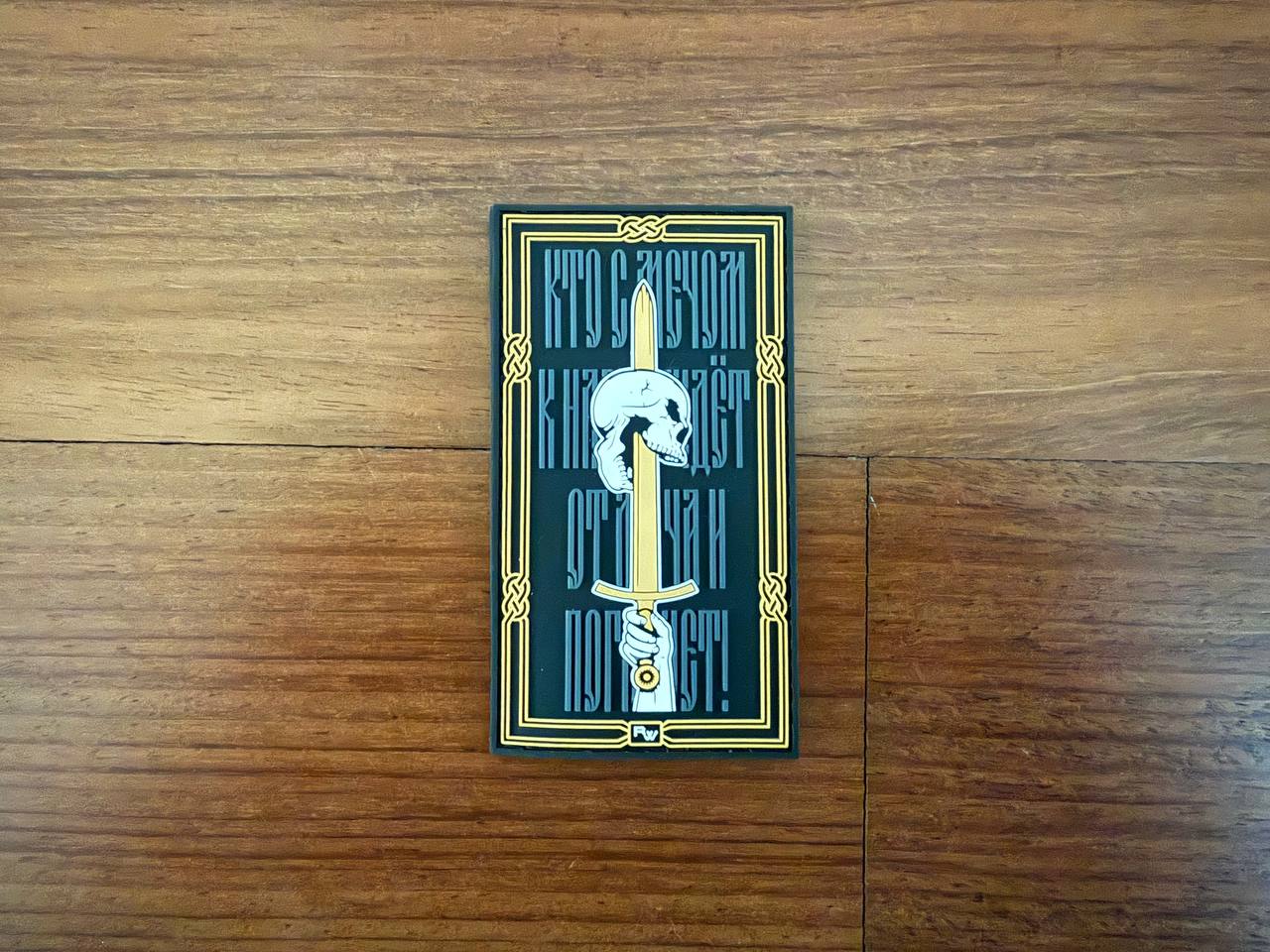 A rectangular Tanki Store patch, Whoever comes to us with a sword, will die by the sword!, shows a stylized knife, white animal skull, and ornate Cyrillic text—ideal for tactical badge collectors or adding to your set.
