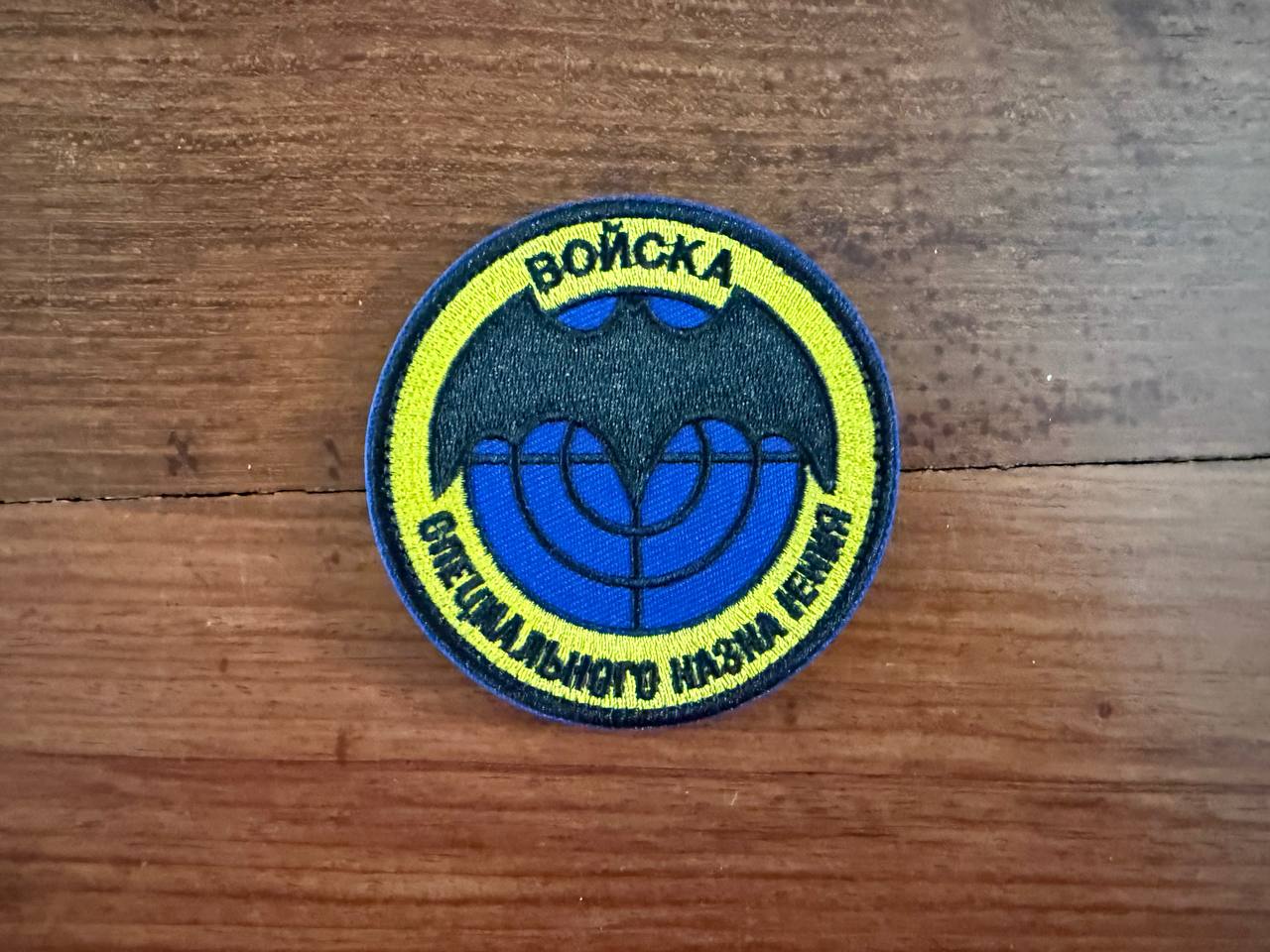 Circular patch with text and blue emblem on a wooden surface