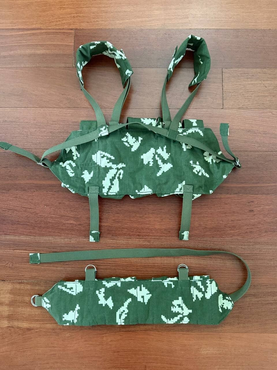 Camouflage chest rig and belt on a wooden floor.