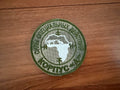 Circular patch with text and a map on a wooden surface