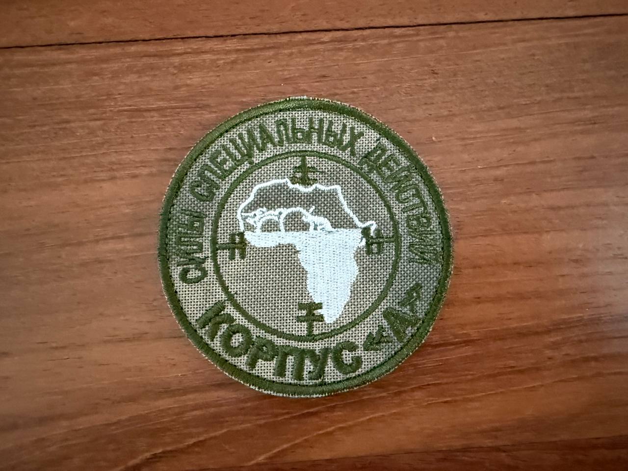 Circular patch with text and a map on a wooden surface