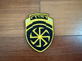 Shield-shaped patch with yellow and black design on a wooden surface