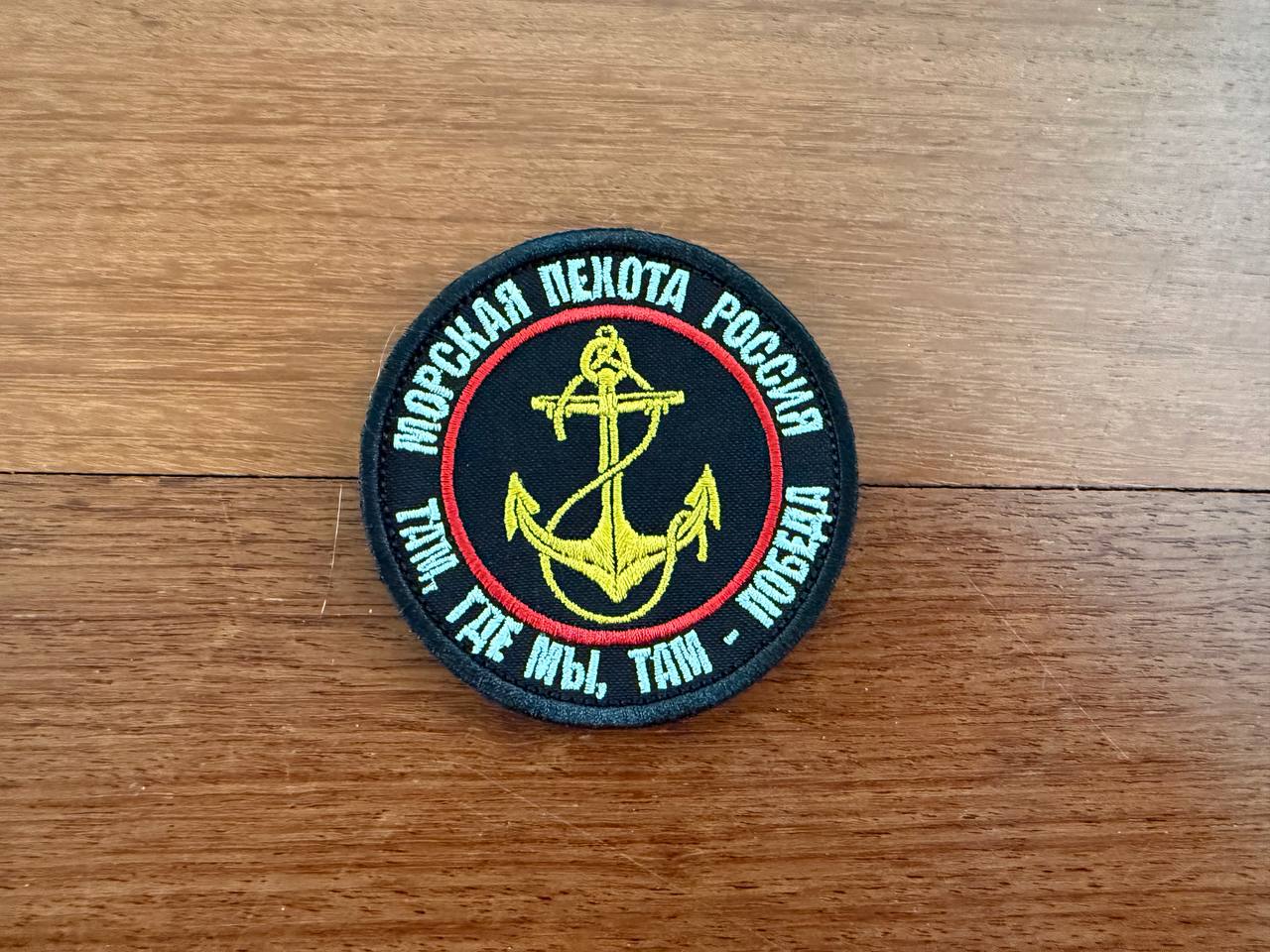 Circular patch with anchor design and text on a wooden surface