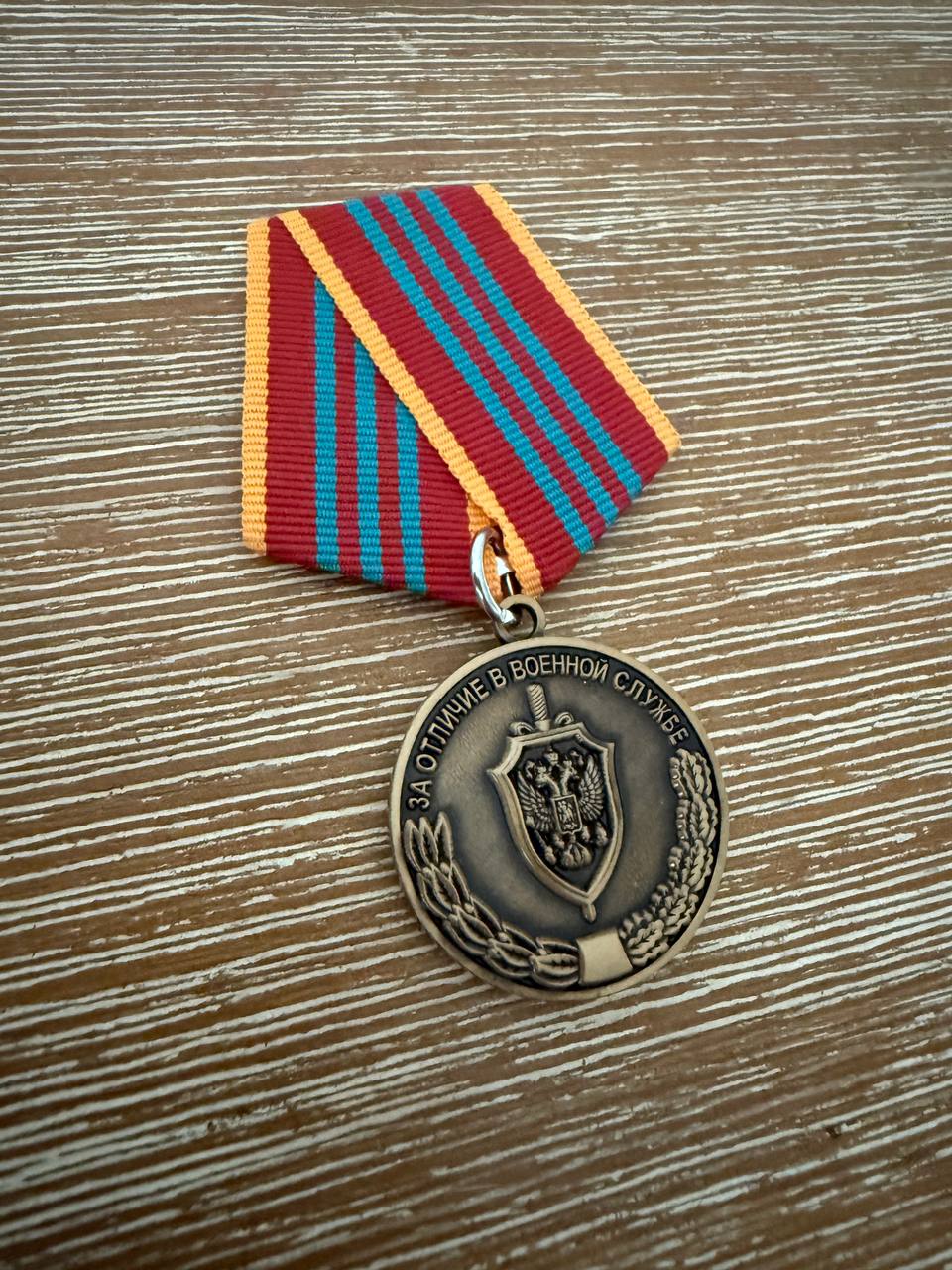 Close-up of a Russian FSB Medal "For Distinction in Military Service" - Replica, featuring a red and blue striped ribbon and detailed emblem on a wooden surface.