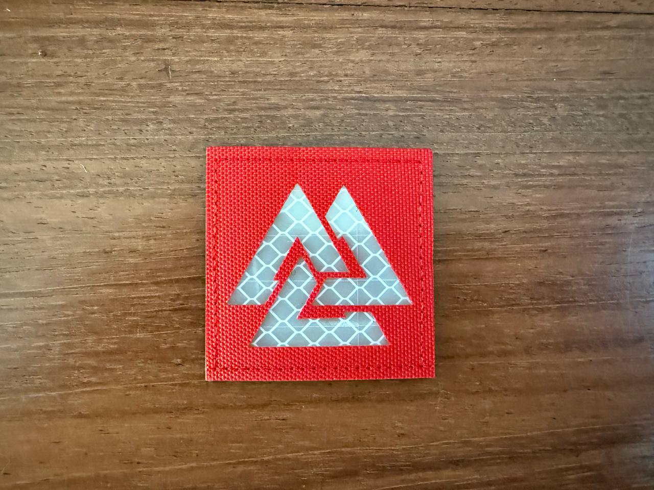 Russian Valknut Slavic/Norse Symbol 2x2' - Military Patch with a reflective silver Valknut design on a red fabric background, displayed on a wooden surface.