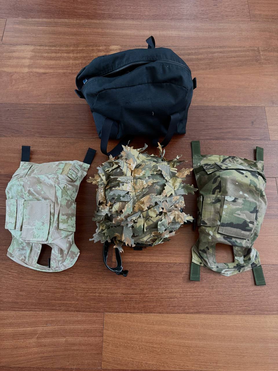 Black tactical helmet with three camouflaged covers including a leaf pattern, displayed on a wooden floor featuring the Russian LSHZ 1+ Helmet Size 2 + Team Wendy Upgrade + FSB Contract Leaf Cover.