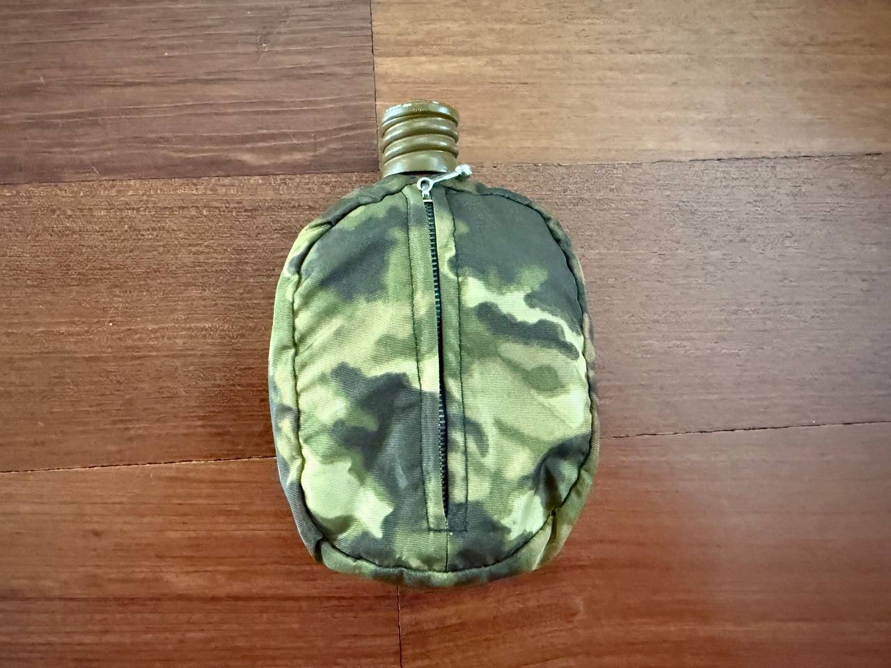Russian Soviet Army Aluminum Water Flask (Canteen) with Camo Cover resting on a wooden surface, featuring a green and brown camouflage pattern and a metal screw cap.