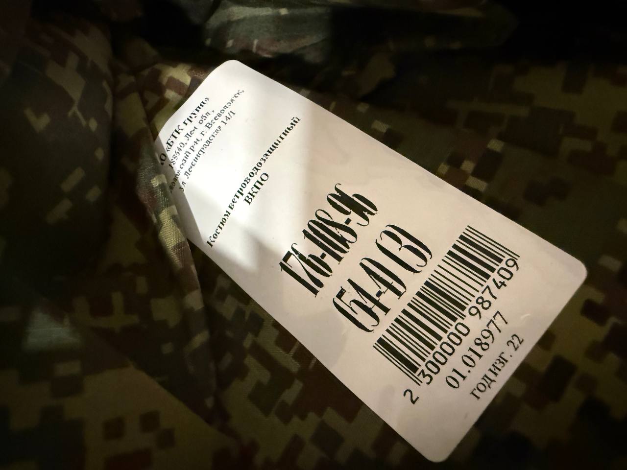 Close-up of a size label on a camouflage fabric showing a tag for Russian BTK Group VKPO Layer 6 Waterproof Windproof Suit - EMR Camo, Size 54-4, highlighting the Russian surplus military clothing from Tanki Store.