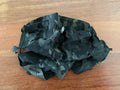 Russian Black Multicam Leaf Helmet Cover laid out on a wooden surface, featuring black and dark green camouflage pattern with drawstrings for secure fit.