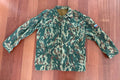 Russian VSR-93 Summer Jacket – Size 52/4 in green and brown Russian surplus camouflage pattern with front pockets and a Russian flag patch on the sleeve laid flat on wood background.