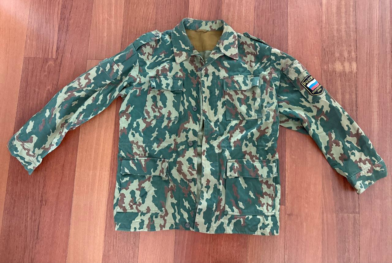 Russian VSR-93 Summer Jacket – Size 52/4 in green and brown Russian surplus camouflage pattern with front pockets and a Russian flag patch on the sleeve laid flat on wood background.