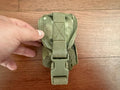 Hand holding a compact Russian Ana Tactical Single Grenade Pouch - Multicam - Old Gen FSB made of durable fabric on a wooden surface, showcasing its secure buckle closure.