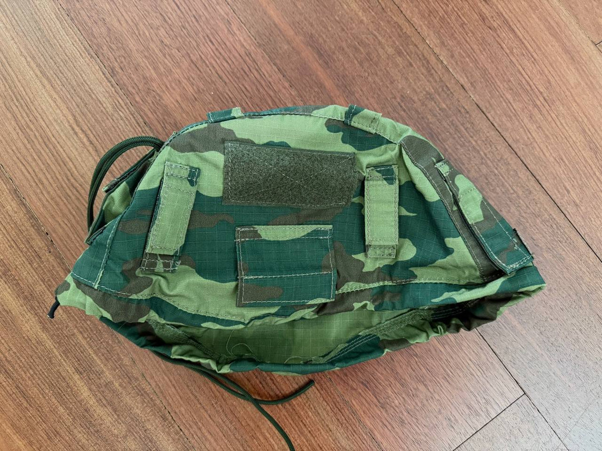 Russian 6b47 Helmet Cover - VSR98 - Size 2 in green and brown camouflage pattern lying flat on a wooden surface, showcasing fabric texture and attachment straps.
