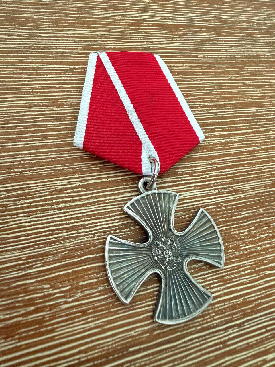 Russian Order of Courage for Military Merit - Replica featuring a silver cross medal with a red and white ribbon, displayed on a wooden surface.