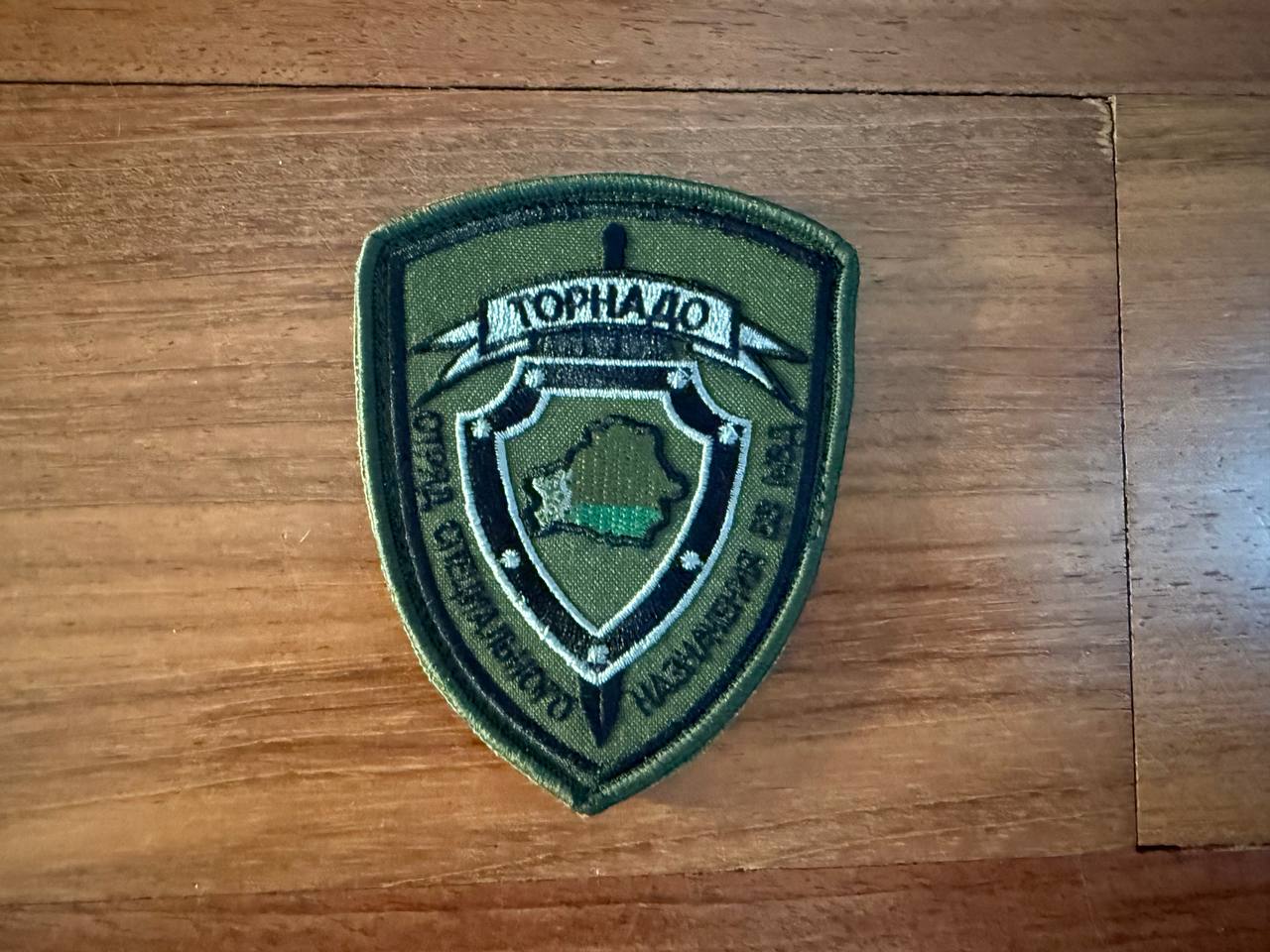 Belarus Spetsnaz "Tornado" Special Forces - Military Patch featuring an embroidered shield emblem with Cyrillic text on an olive green background, displayed on a wooden surface.