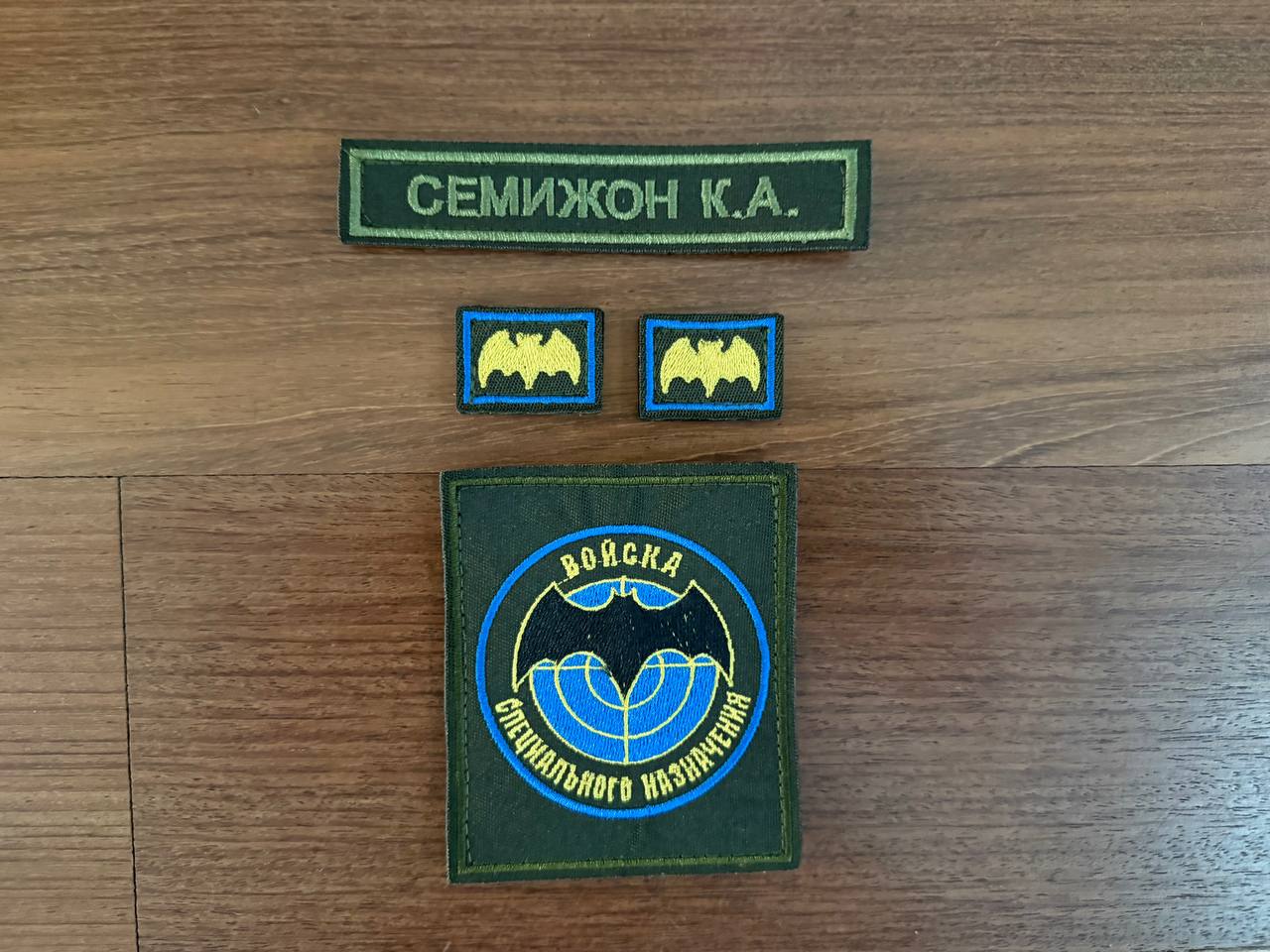 Russian GRU Spetsnaz (Random Russian Names) - Military Patch Set featuring green name patch and several insignia with bat and globe designs on wooden surface, Russian surplus style.