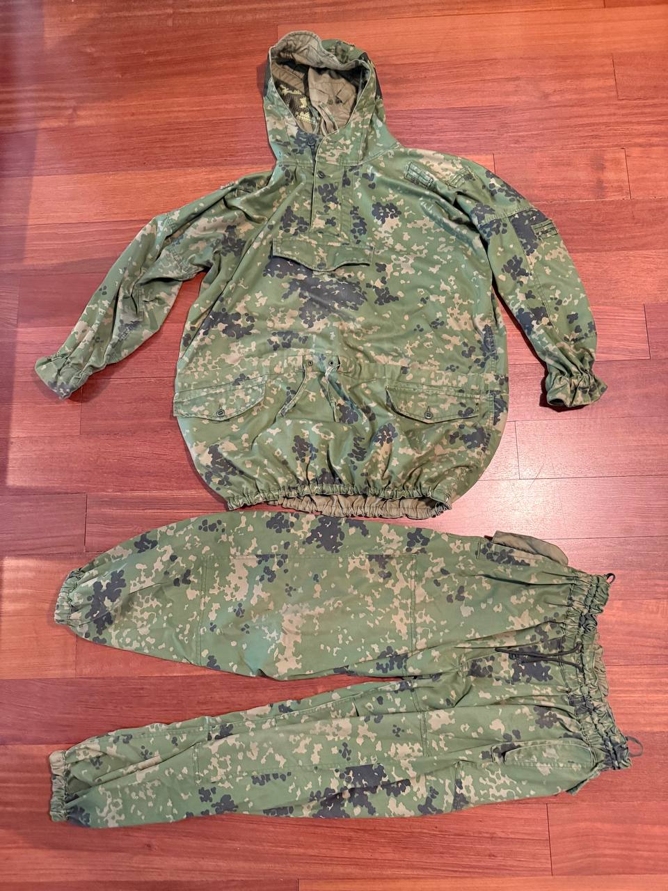 (USED) Russian SSO Partizan Sever Suit - Size 56-58/5 displayed on a wooden floor, featuring a green digital camouflage pattern with a hooded jacket and matching pants, typical of Russian surplus gear.