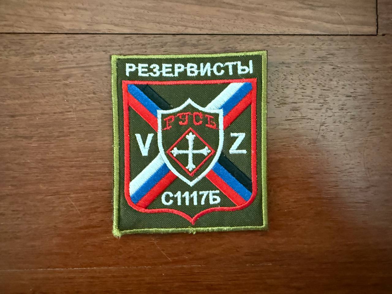 Patch displaying a shield with a cross and Cyrillic letters, bordered by red, blue, white, and black diagonal stripes, with the text "Russian DNR Rus Separate Battalion - Military Patch" above and below on an olive background.