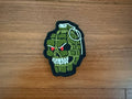 Russian Tactical Grenade Skull - Military Patch featuring an embroidered green grenade with a skull face and red eyes, designed on a wooden surface background.