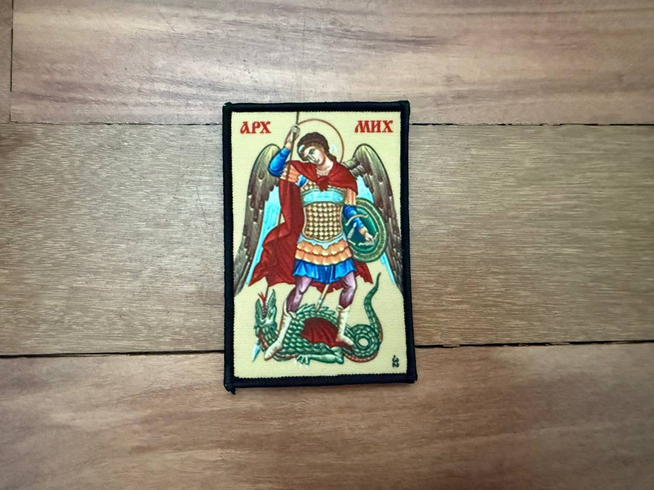 Decorative patch with an angel and dragon design on a wooden surface