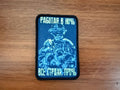 Blue patch with a person wearing night-vision glasses  and text on a wooden surface