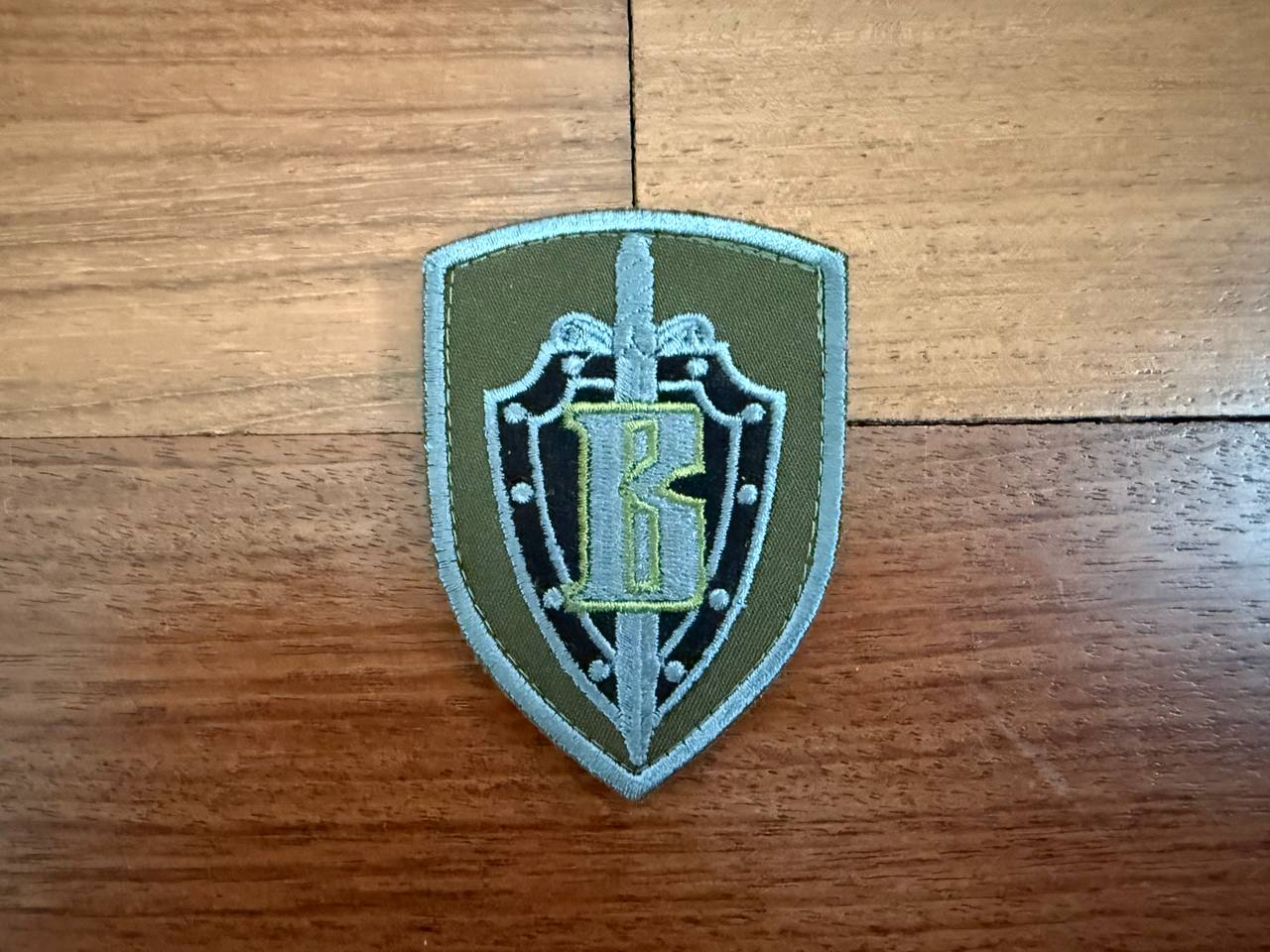 Shield-shaped patch with a logo on a wooden surface