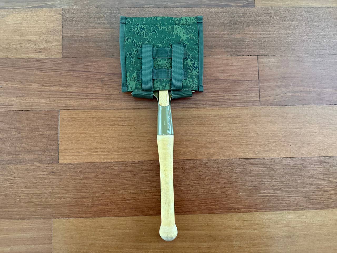 Russian Military Shovel & Tekhinkom Shovel Pouch Set displayed on a wooden surface, featuring a wooden-handled shovel with a green camouflage pouch attached for easy carrying.