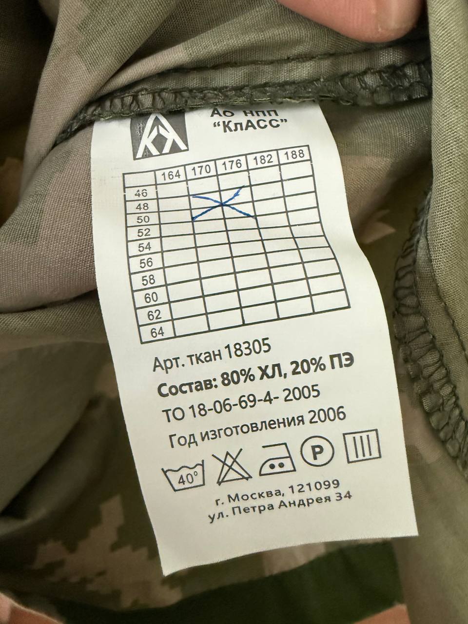 Close-up of a clothing label on a Russian AO NPP Klass White Breaks Suit - Size 48-50/3-4 showing fabric composition, care instructions, and sizing chart with handwritten marks.