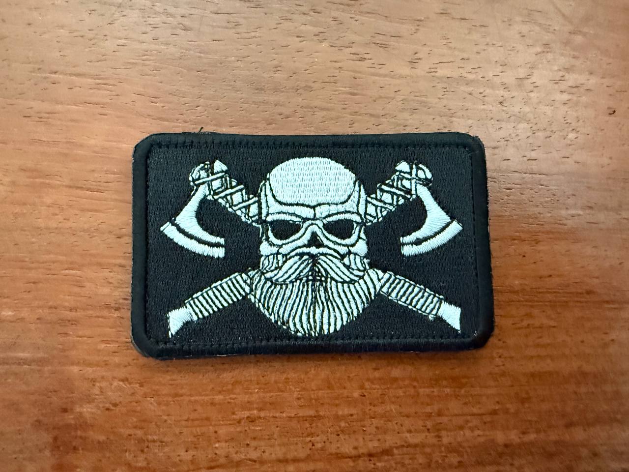 Close-up of a Russian Viking White Toned - Military Patch featuring a skull with a beard and crossed axes on a black background, showcasing detailed embroidery.