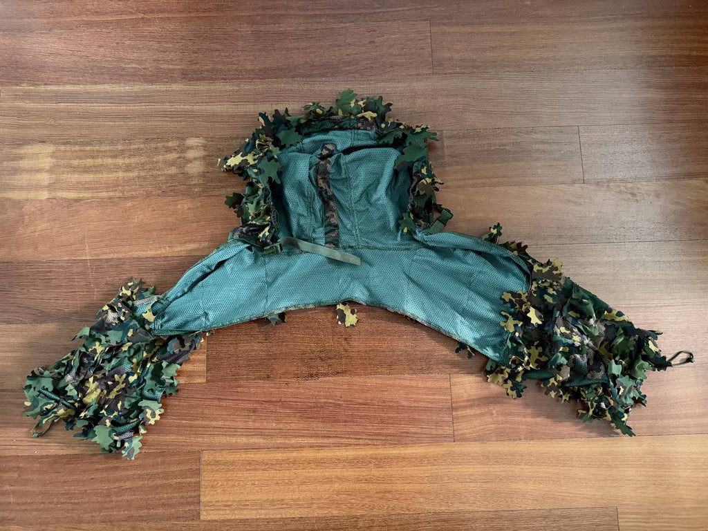 Green and brown camouflage Russian SS-Leto Leaf Cape / Viper Hood with leaf-like fabric pieces designed for concealment, laid flat on a wooden floor.
