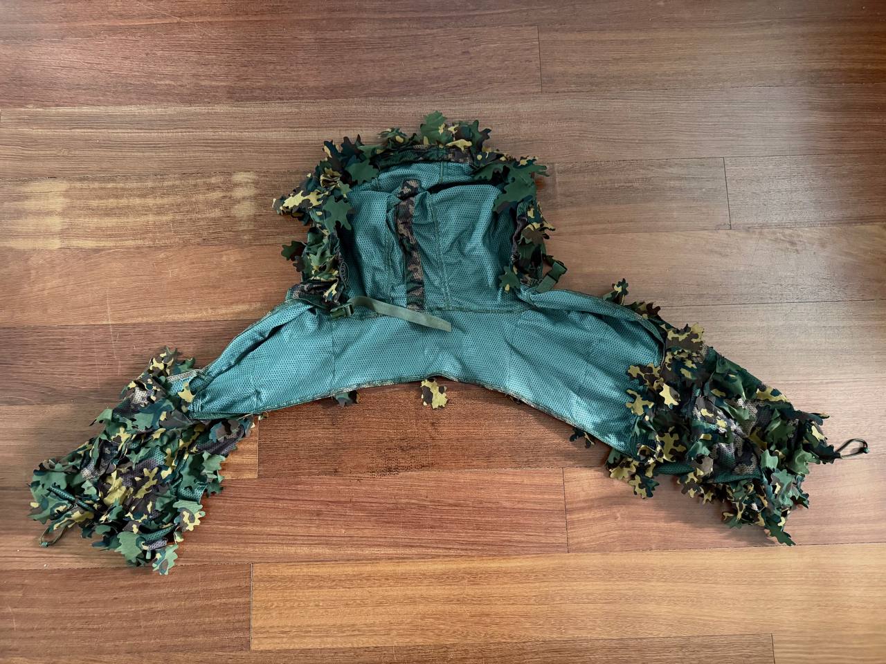 Green and brown camouflage Russian SS-Leto Leaf Cape / Viper Hood with leaf-like fabric pieces designed for concealment, laid flat on a wooden floor.