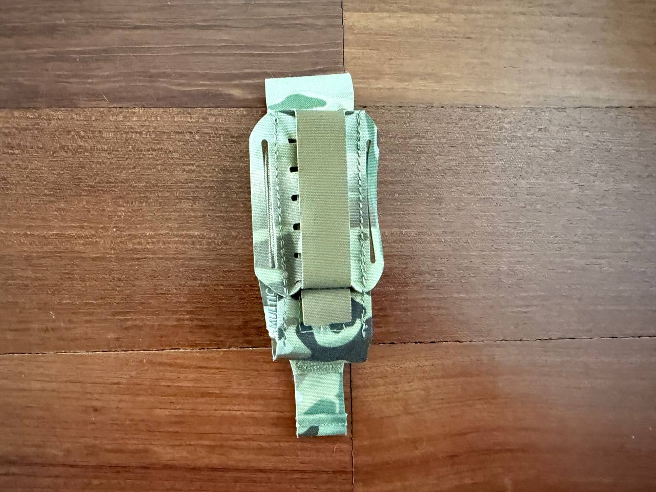 Russian Ars Arma - "Super 86" Laser-Cut Tourniquet Pouch – Multicam (Used) displayed on a wooden surface, featuring a compact design with a sturdy metal clip and camouflage pattern.