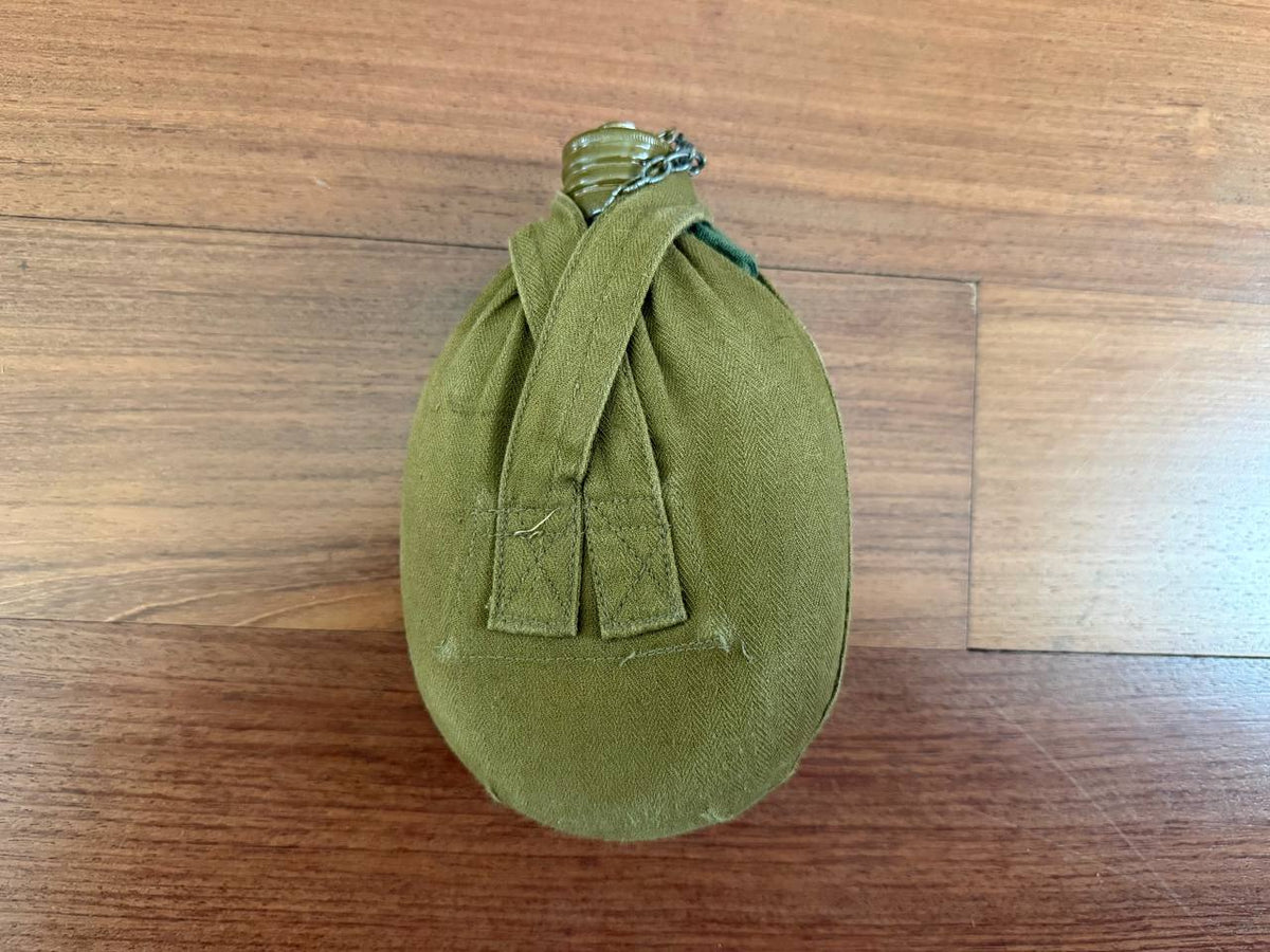 Russian Soviet Army Aluminum Water Flask (Canteen) with Canvas Cover resting on a wooden surface, showcasing its olive-green fabric and metal cap with chain.