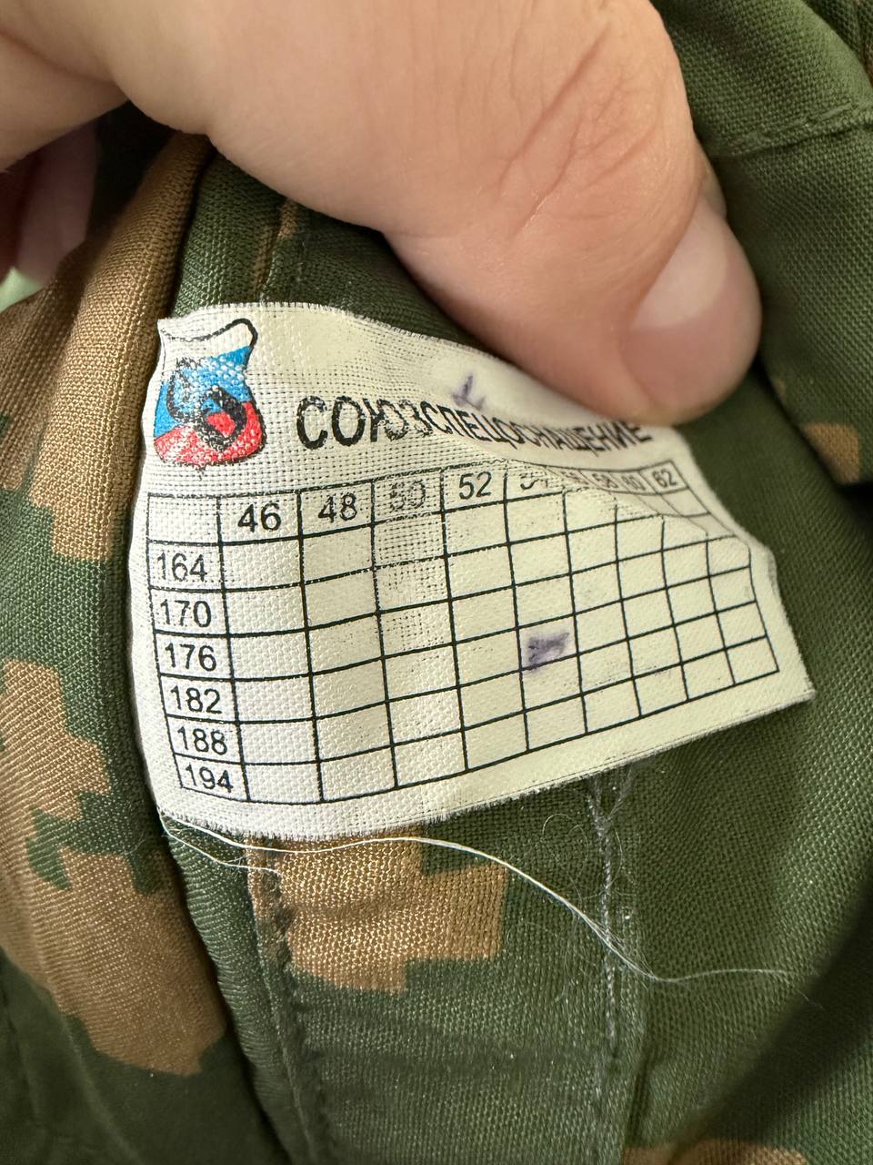 Close-up of a size label inside Russian SSO "Sumrak" Suit – Gold Dubok Color - Size 54-5 showing size chart and Russian text on green camouflage fabric.