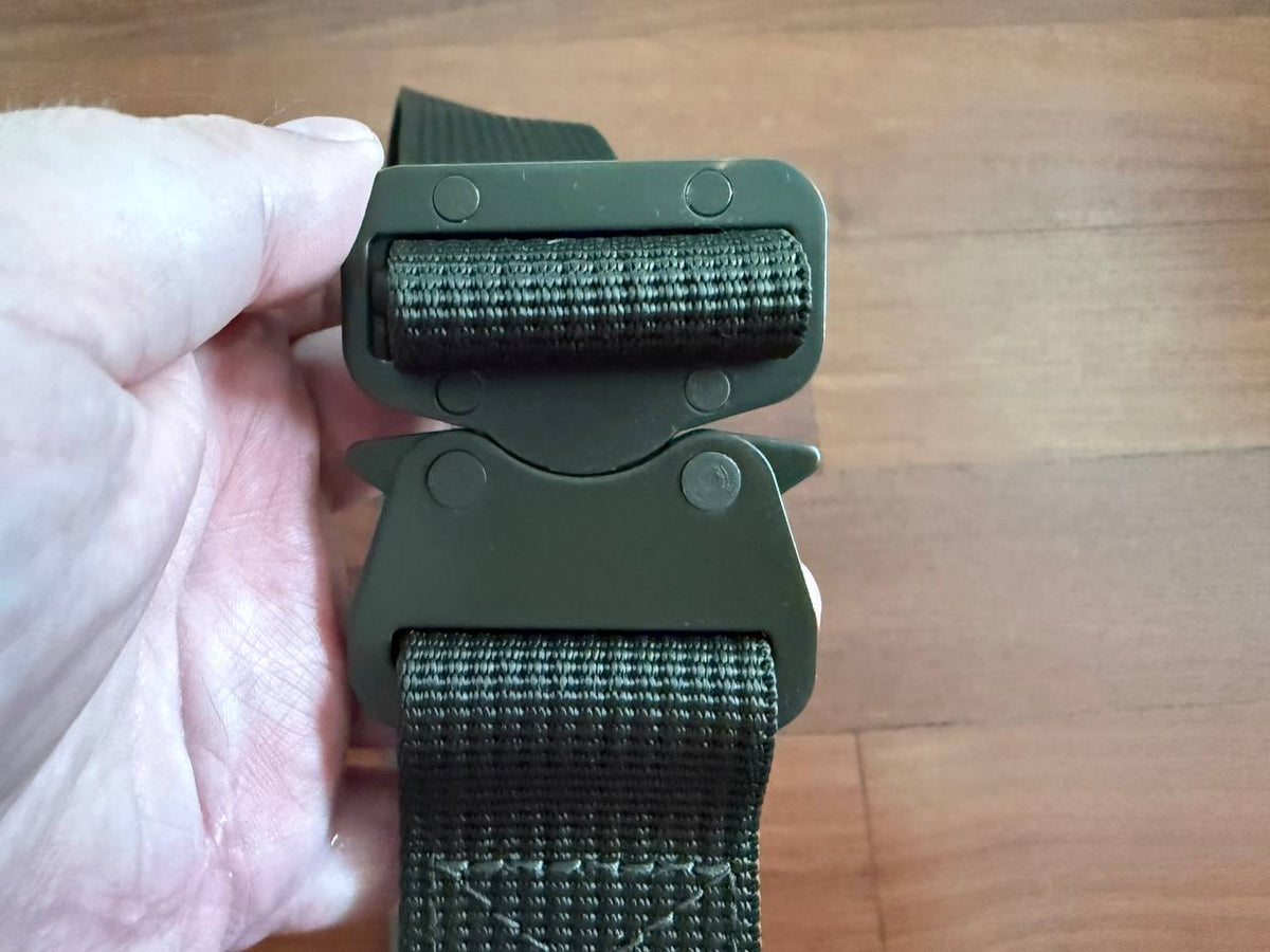 Close-up of a person holding the buckle of the Russian BTK Group - VKPO 3.0 Tactical Belt – Olive Drab, showcasing the durable olive drab webbing and sturdy metal clasp.