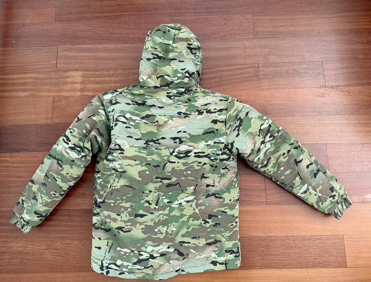 Russian Innovation Cold Weather Jacket (Layer 7) – Multicam - Size 54/5 displayed from the back, showcasing its camouflage pattern and hood on a wooden floor.