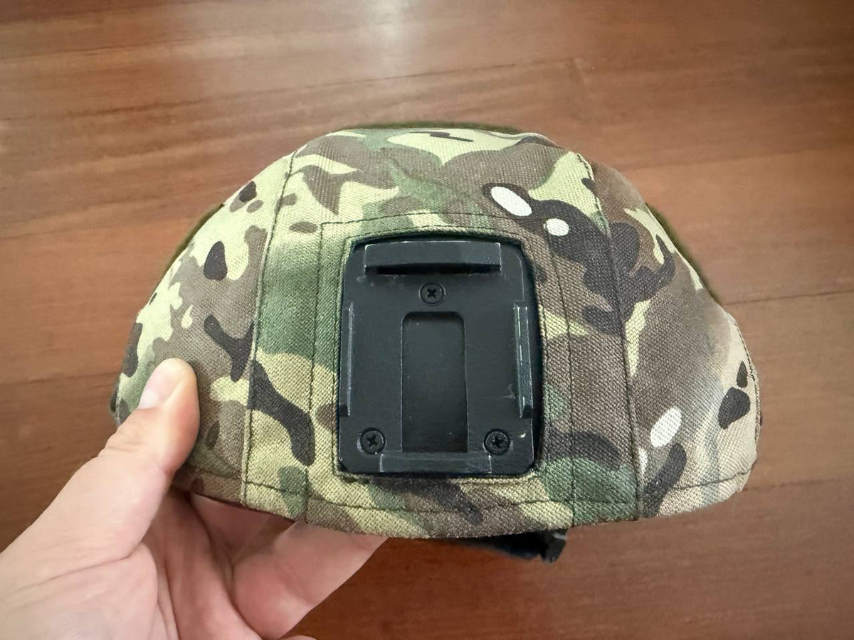 Hand holding a Russian LShZ 1+ Highcut Opscore Helmet - Size 3 + Multicam Cover, showing the back with a mount bracket against a wooden floor background.