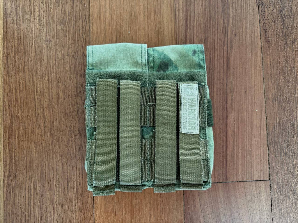 Warrior Assault Systems 4-Cell Mag Pouch - A-TACS FG Camo - Russian Style in green and tan camouflage, designed for secure magazine storage with adjustable straps on a wooden surface.