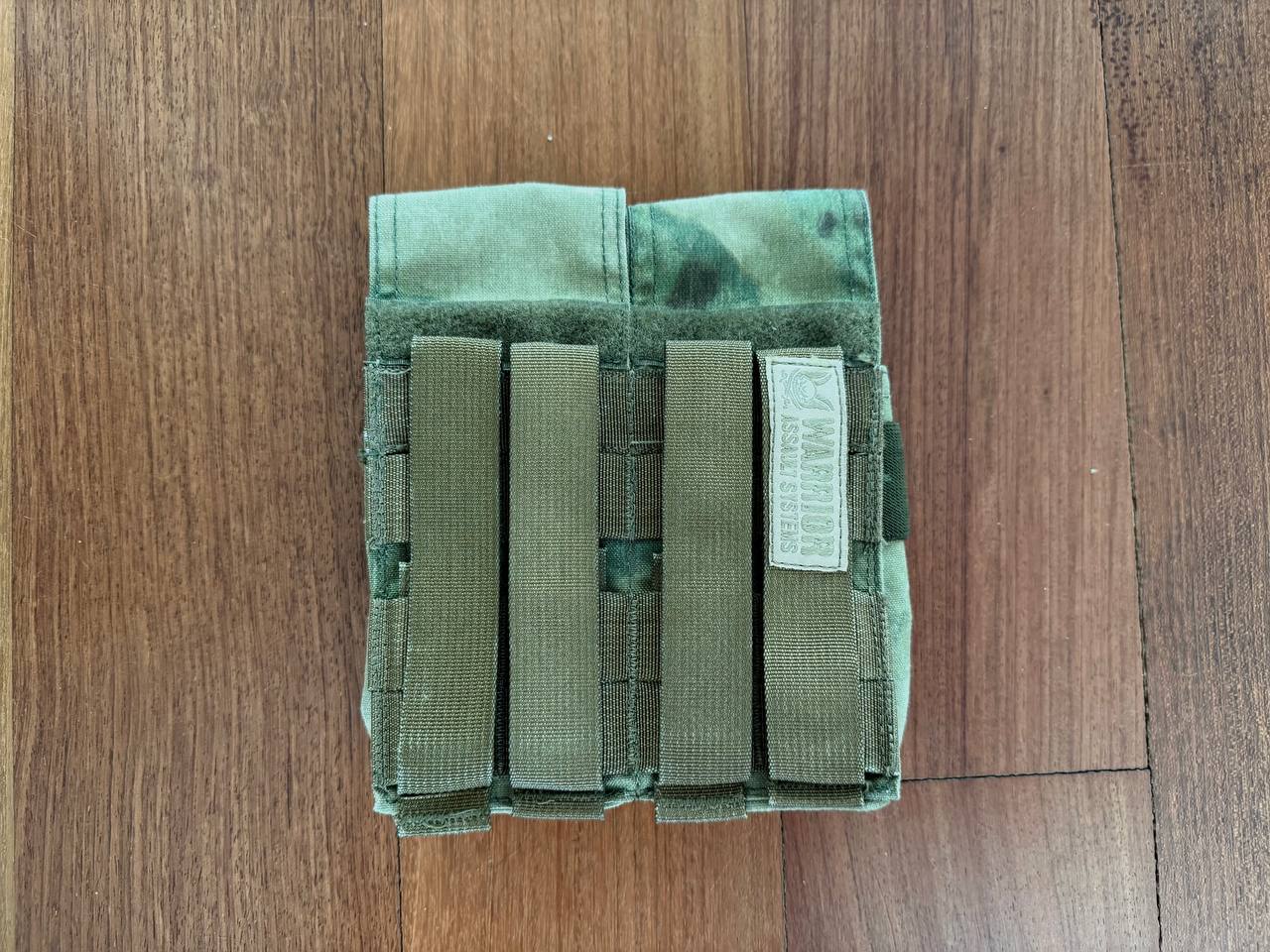 Warrior Assault Systems 4-Cell Mag Pouch - A-TACS FG Camo - Russian Style in green and tan camouflage, designed for secure magazine storage with adjustable straps on a wooden surface.