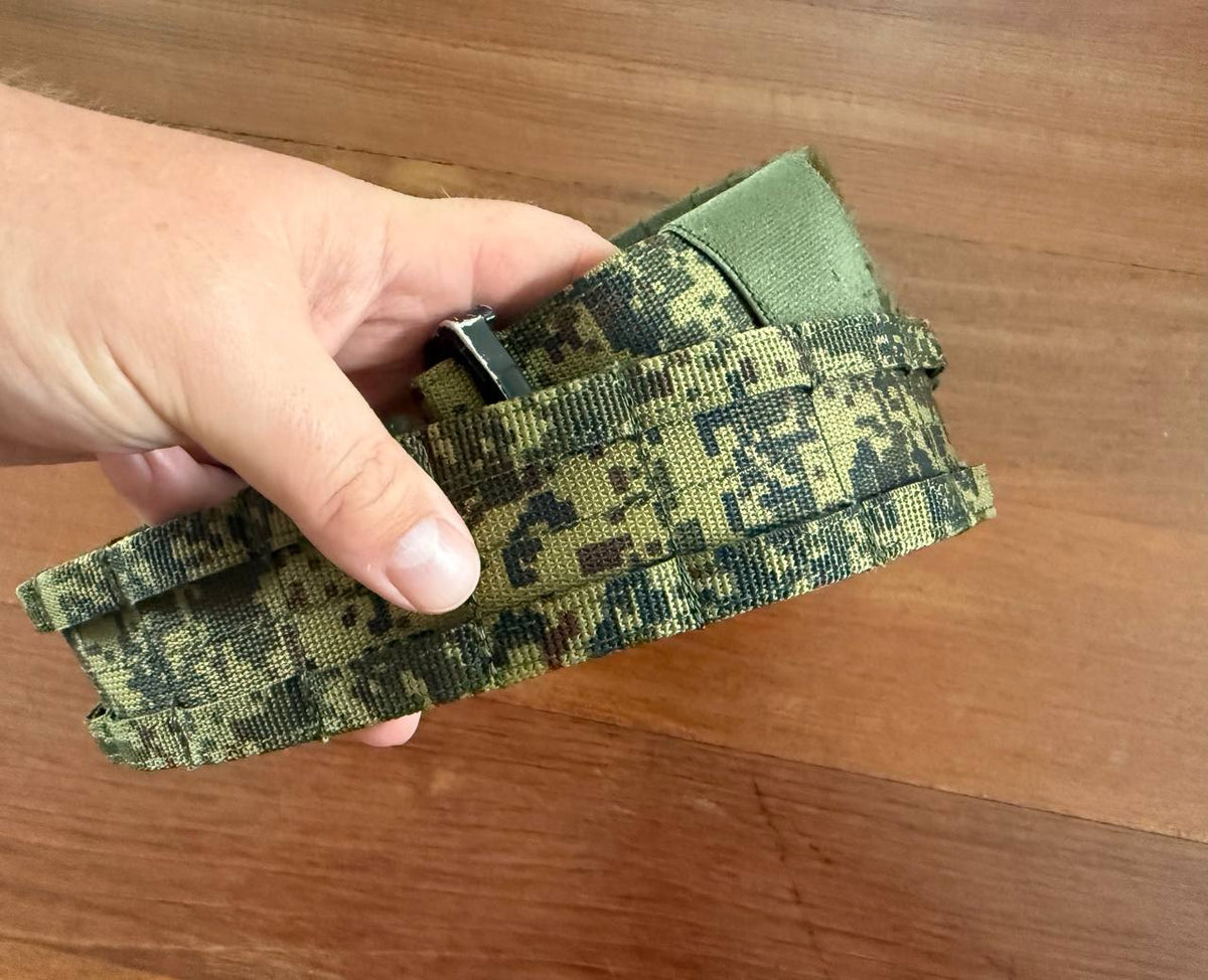 Hand holding a folded Russian Ars Arma Ronin Tactical Belt - EMR - L in digital camouflage pattern against a wooden background.