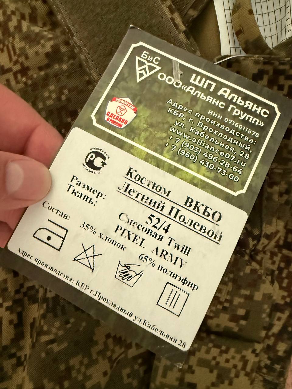 Close-up of a care and composition label on a camouflage fabric showing 35% cotton and 65% polyester blend, labeled Russian Alliance Group Layer 4 Summer Suit (Commercial Prod.) - EMR - Size 52/4.