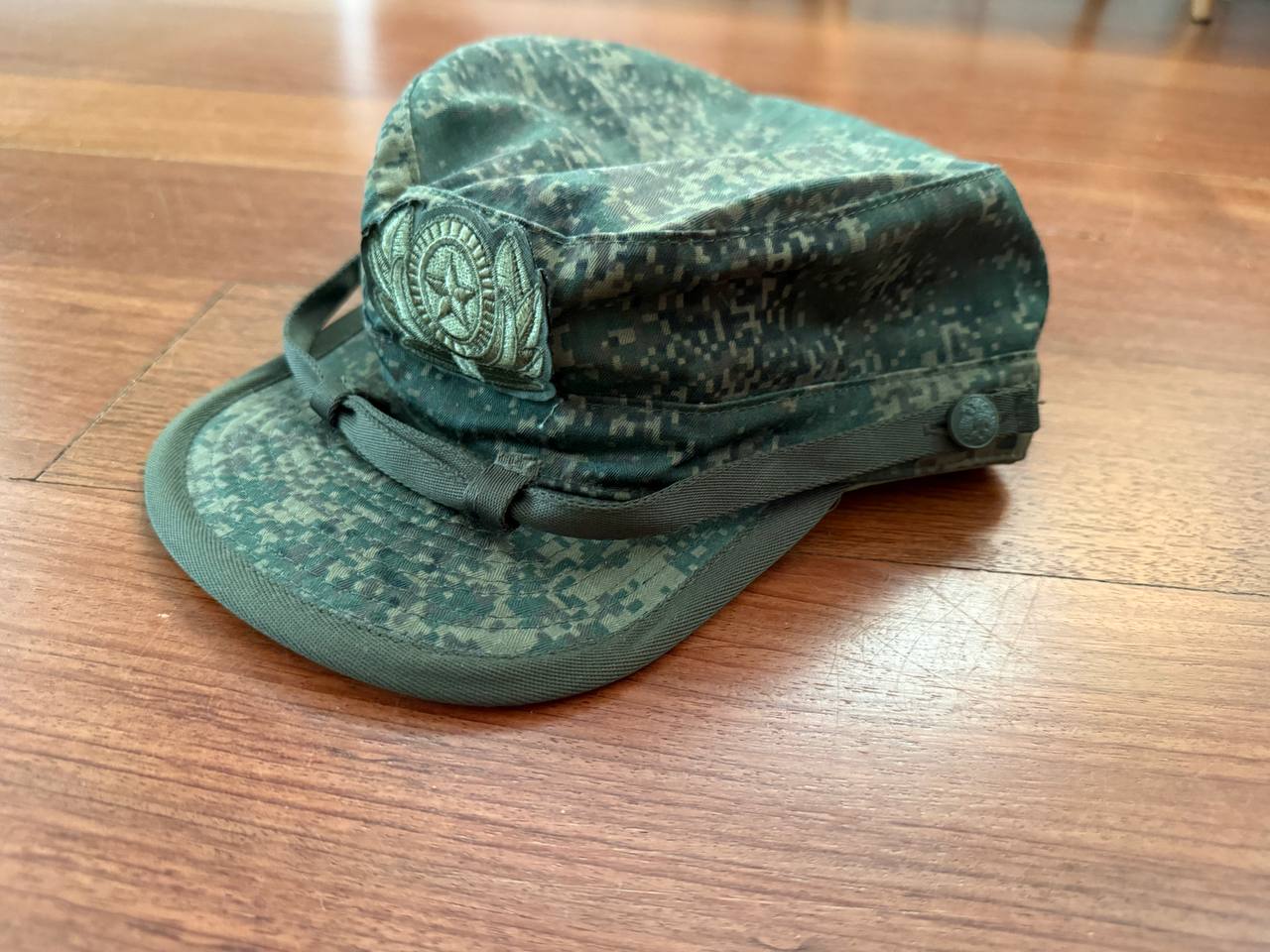 (USED) Russian BTK Group VKBO Cap - EMR Digital Flora - Size 62 in Russian surplus camouflage pattern, featuring a flat top and sewn insignia on front, displayed on wooden surface.