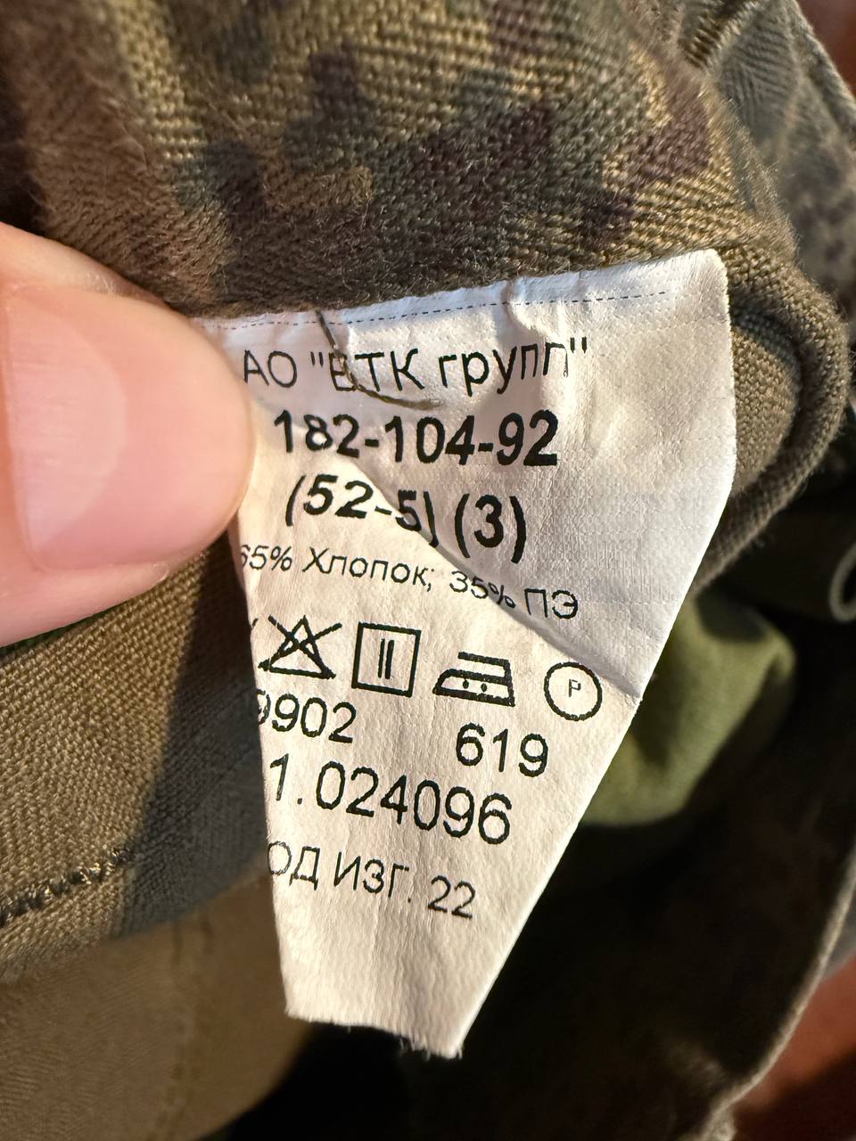 Close-up of a fabric care label on a camouflage garment, showing washing and ironing instructions for the (USED) Russian Army VKPO Layer 4 Summer Suit - EMR Digital Flora - Size 52/5, highlighting Russian surplus military material.