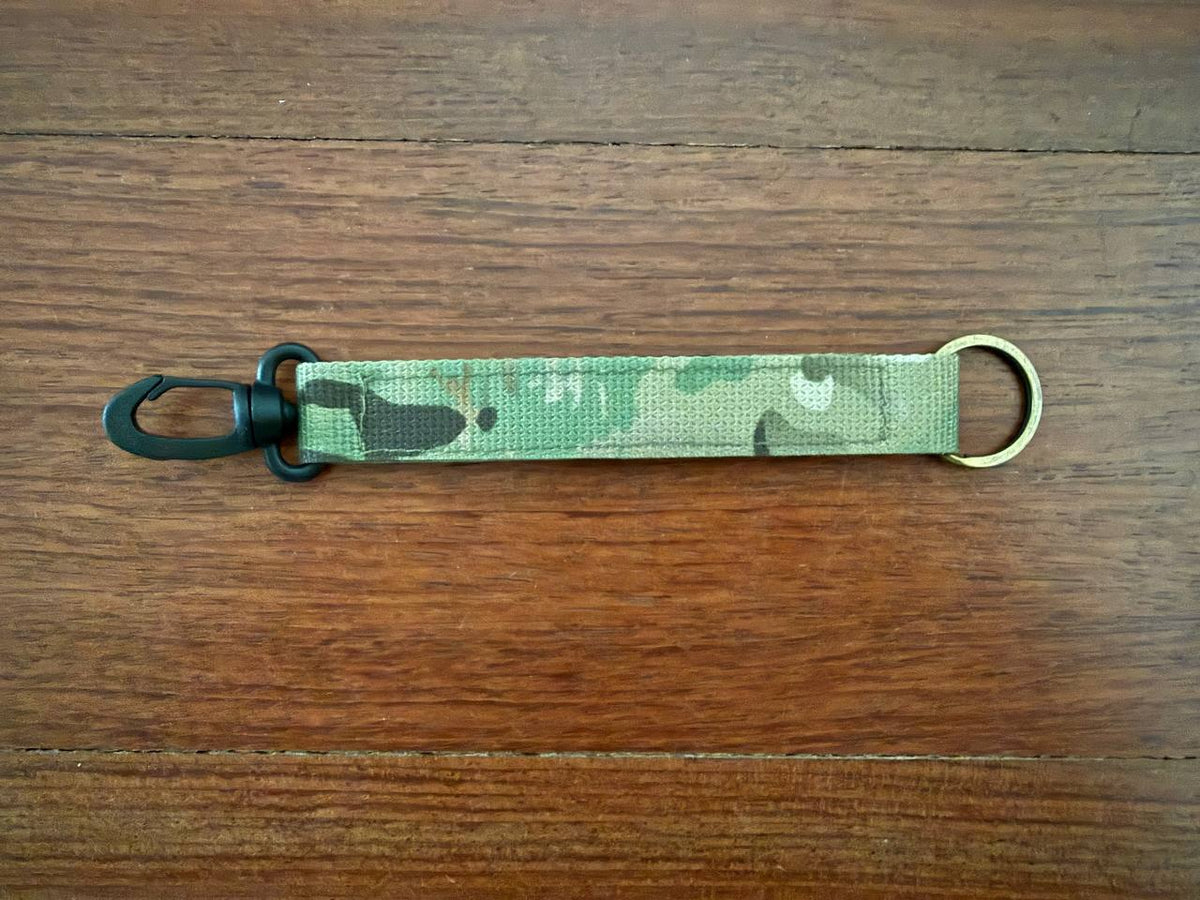 Russian Viking Gear Keychain Lanyard Belt Clip - Multicam with a durable camo fabric strap, black plastic clip on one end, and metal ring on the other, lying on a wooden surface.