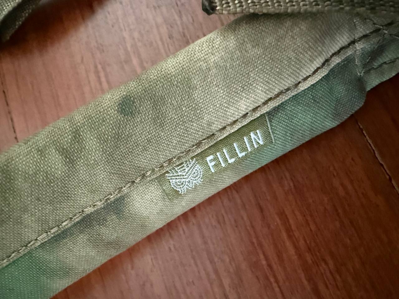 Close-up of a rugged green fabric strap with the Fillin logo, part of the Russian Fillin Tactical Two-Point Gun Sling - A-TACS FG Moss, showcasing durable stitching and material.
