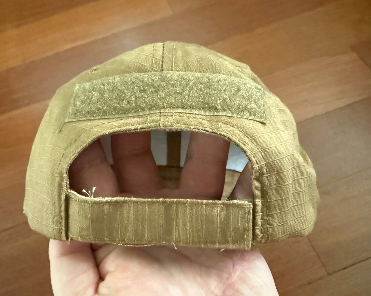 Back view of a Russian Tactical Cap - Tan Color showing the adjustable strap and Velcro patch on a wooden floor background.