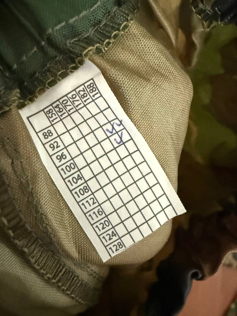 Close-up of a size and measurement label inside a garment, showing multiple size options on a white tag stitched to beige fabric, for the (USED) Russian Layer 6 Waterproof Windproof Suit - Size 96-100/182-188.