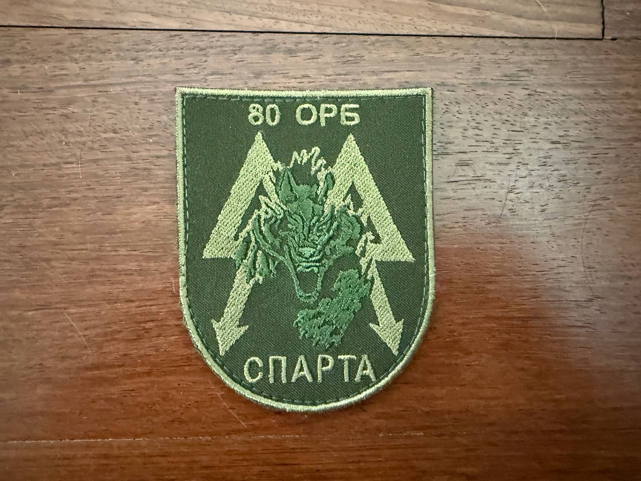 Russian 80th Independent Guards Sparta Battalion - Military Patch featuring a green embroidered dragon head with arrows and Cyrillic text on an olive background, displayed on wood.