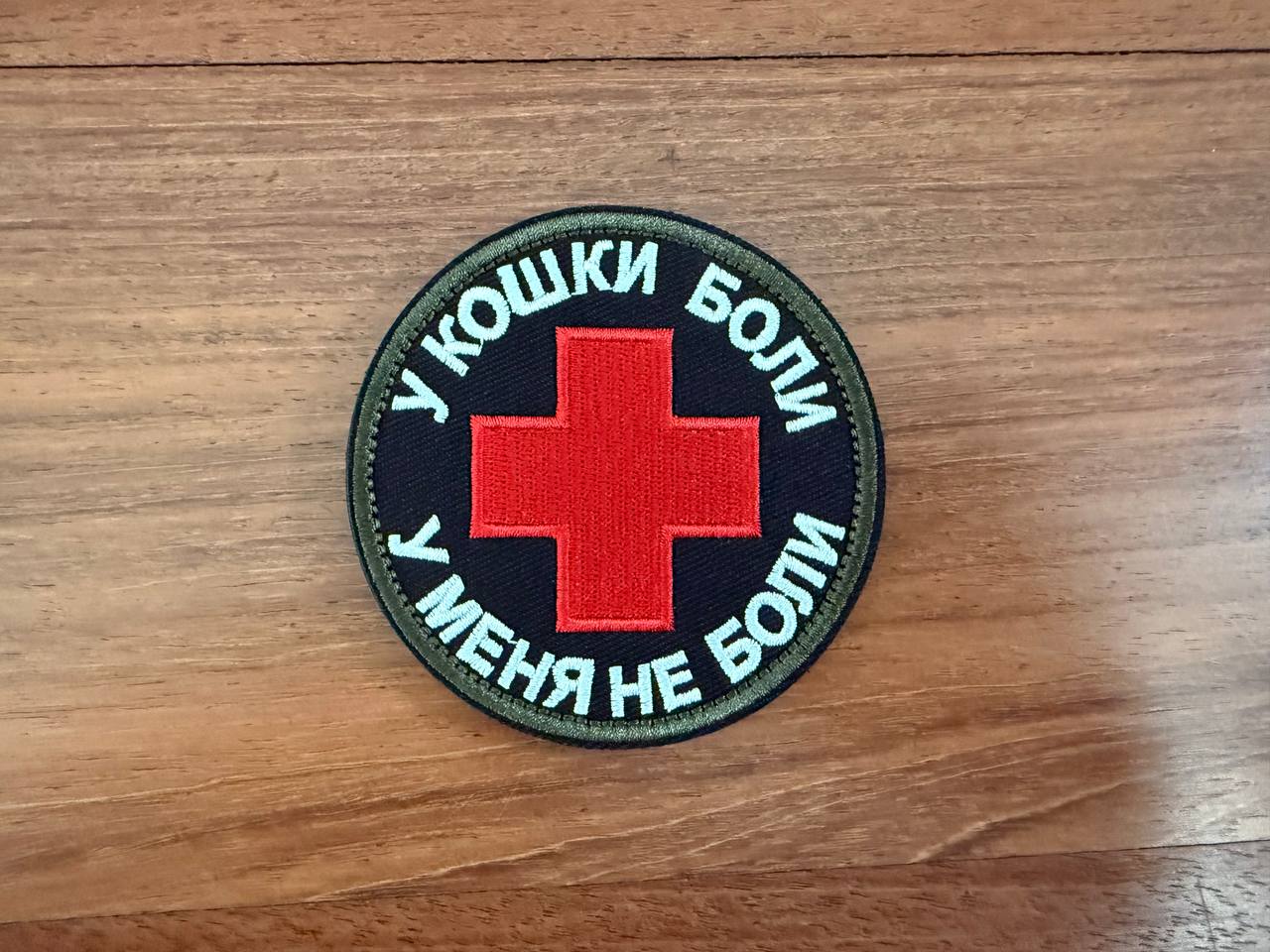 Round patch with red cross and text on a wooden surface