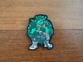 Decorative patch of a character with green and gray design on a wooden surface